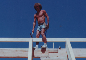 Todd Coash, president of 
NORTH STAR CONSTRUCTION & REMODELING CO. INC. CRC1330674, standing on the roof ridge of a log construction house. He was lead carpenter of this job of a crew of four. He is standing on top of a custom engineered corbel. Used to distribute the load more evenly. Circa. 1992